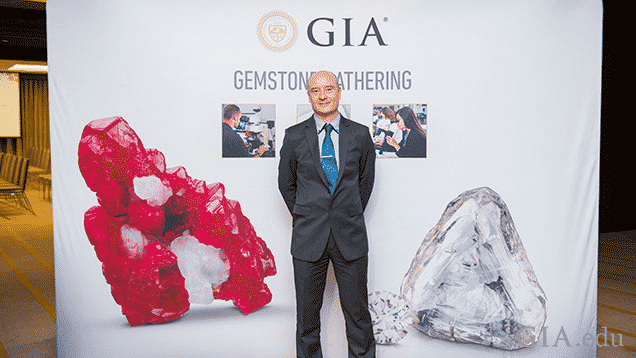 El hombre se para frente a una pancarta de GIA con gemas.